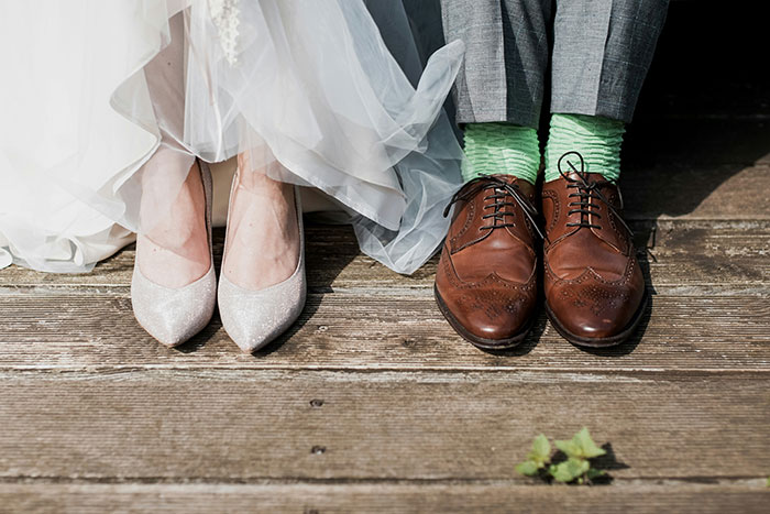 Bride in white shoes and groom in brown shoes with green socks on wooden boards, symbolizing marriage differences.