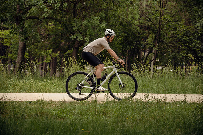 Person cycling on a path through a green park, wearing a helmet and athletic gear, showcasing signs of healthy living.