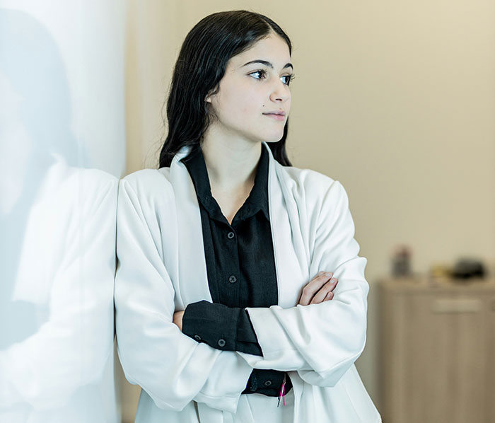 A woman in a white suit, arms crossed, looking contemplative, represents signs a marriage is destined to fail.