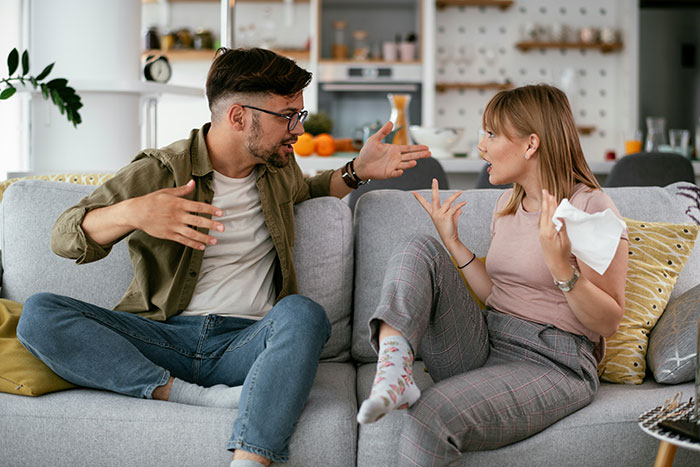 Couple arguing on sofa, showing marriage issues, with expressive gestures in a home setting.