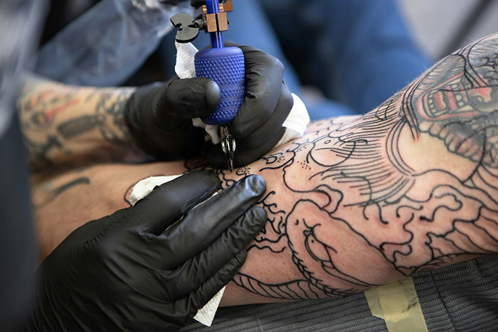 Tattoo artist working on a detailed leg design, possibly illustrating signs of marital distress.