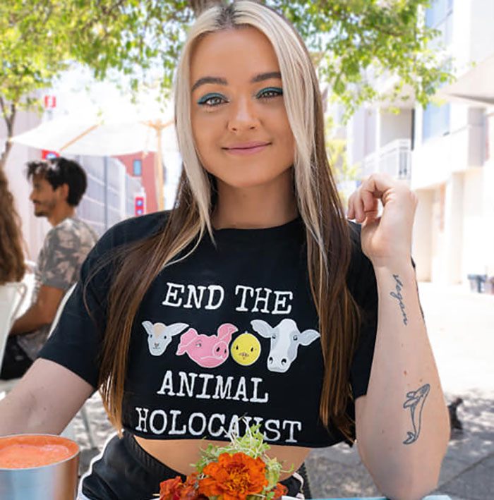 Vegan activist at outdoor cafe wearing a shirt with animal rights message, with bright makeup and tattoo.