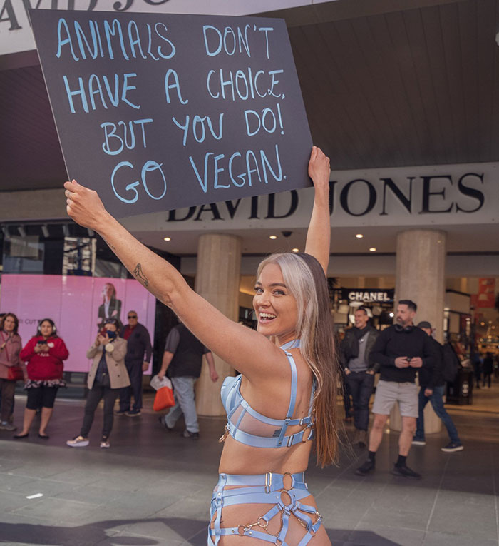 Vegan activist holding a sign promoting animal rights in a public setting.