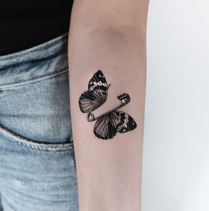 Butterfly tattoo design with a safety pin on a woman's arm, showcasing unique tattoo ideas for women.