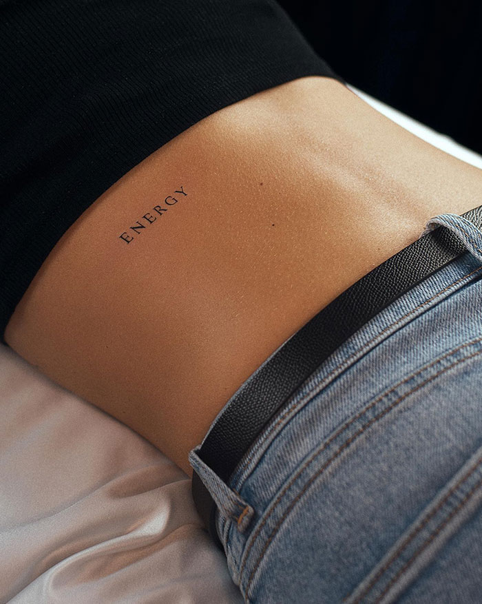 A tattoo idea for women with a lower back tattoo with the word "Energy" on a woman's skin, featuring subtle design.