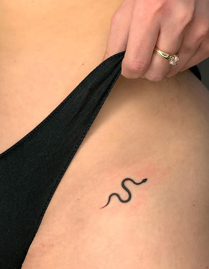 A tattoo idea for women with a minimalist snake tattoo design on a woman's leg.