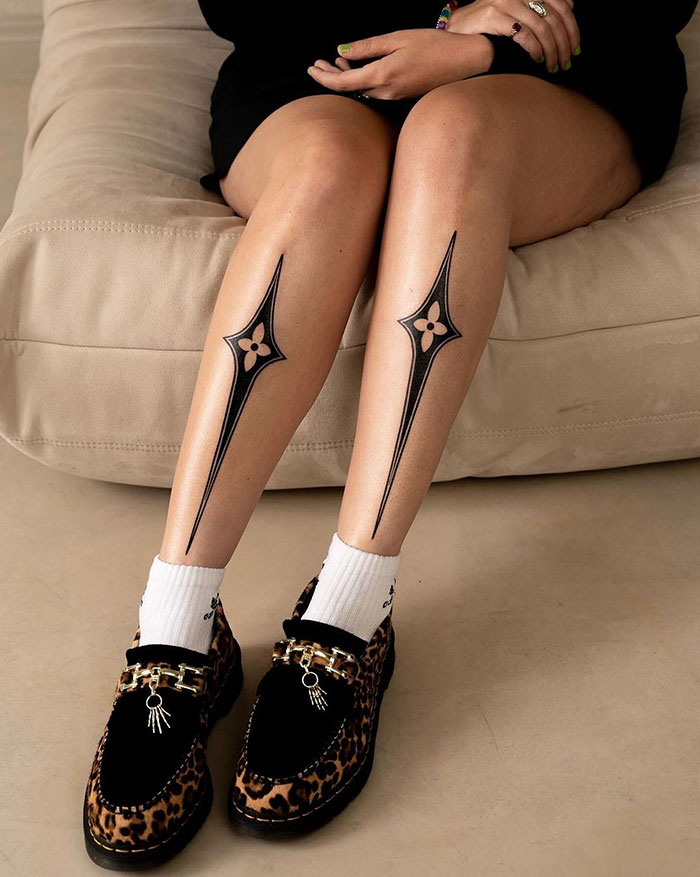 A tattoo idea for women with a geometric tattoo design on woman's legs, featuring bold black lines and floral elements.