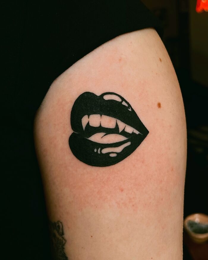 Vampire lips tattoo on an arm, showcasing a bold tattoo idea for women.