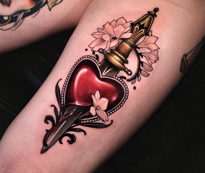 A tattoo idea for women featuring a dagger piercing a heart with floral accents.