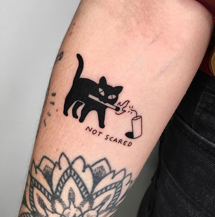 Black cat tattoo on arm with "Not Scared" text, showcasing daring tattoo ideas for women.