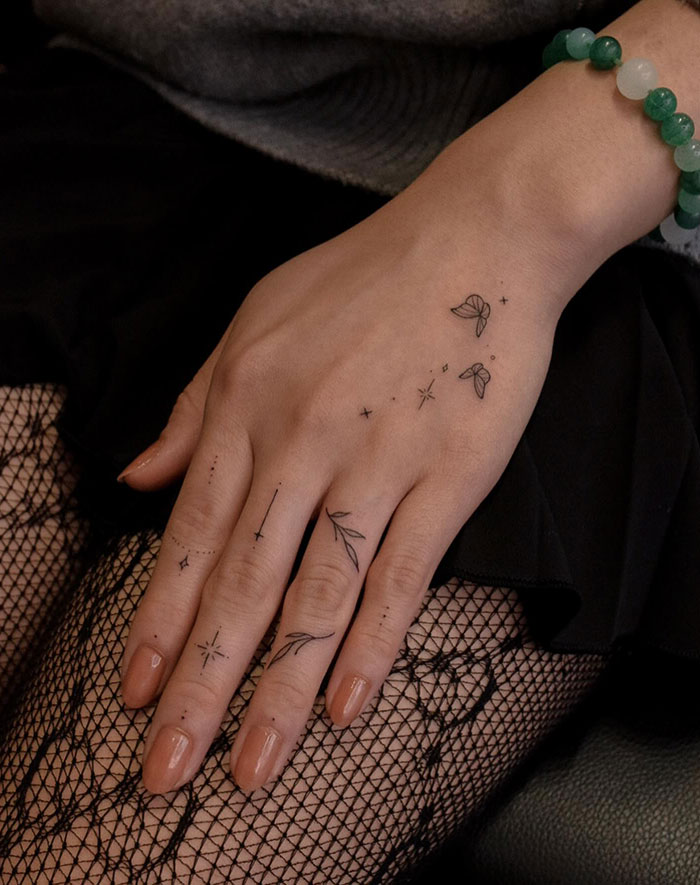 Hand tattoo idea for women featuring stars and leaves, with a delicate design on fingers and wrist.