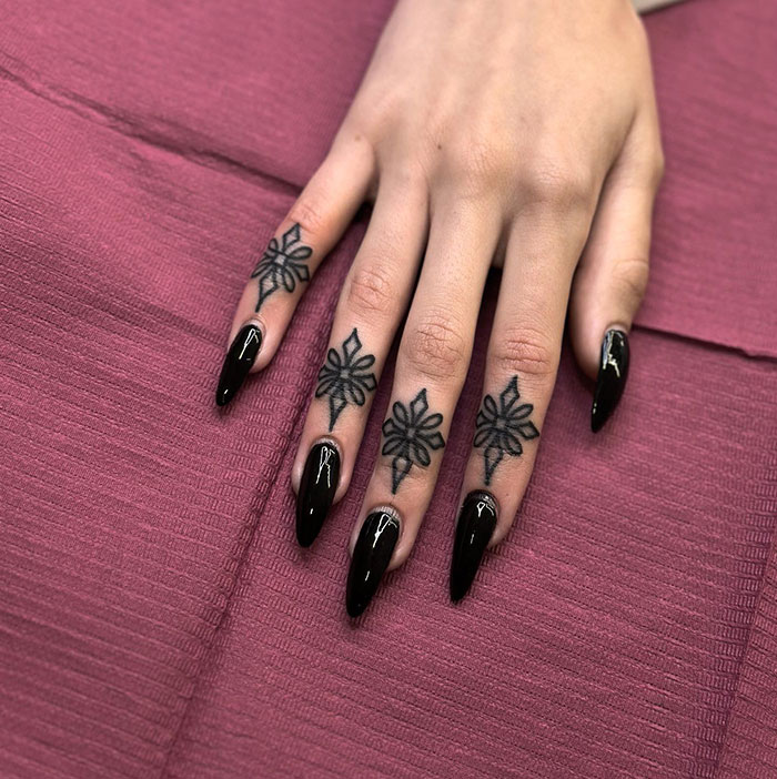 Floral finger tattoos on a woman's hand with black nails, showcasing unique tattoo ideas for women.