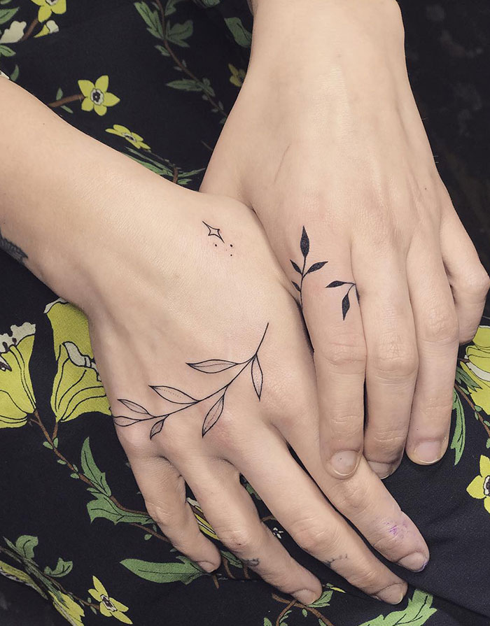 A tattoo idea for women with women's hand tattoos featuring delicate leaf designs on each hand.