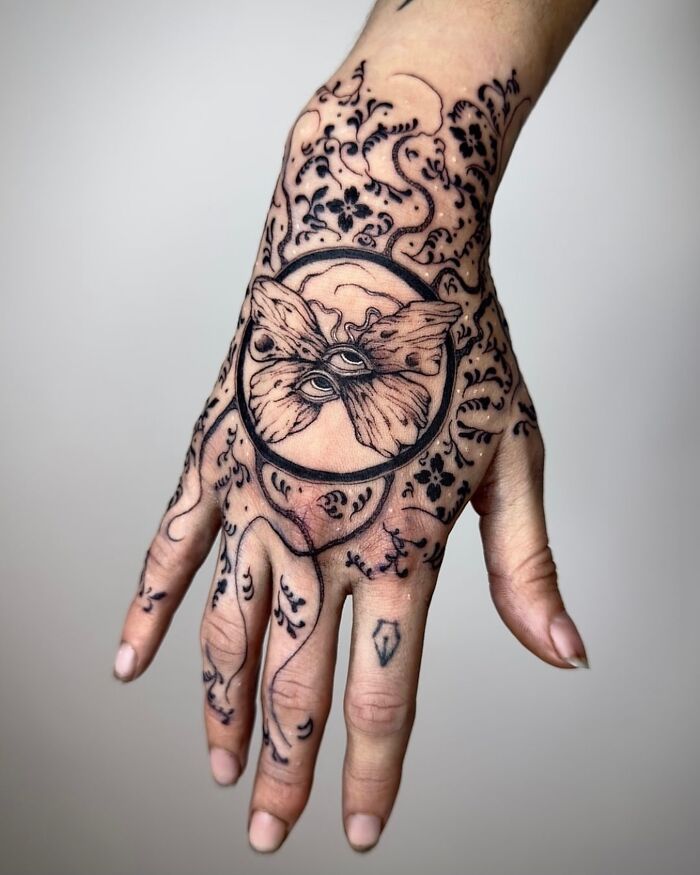 Hand tattoo with intricate designs, featuring a moth and floral elements, showcasing daring tattoo ideas for women.