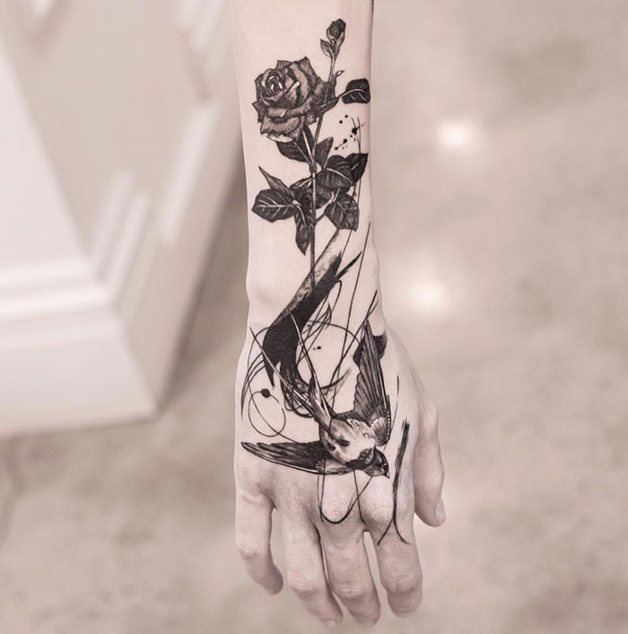 A tattoo idea for women with a black ink tattoo of a rose and bird on a woman's arm.