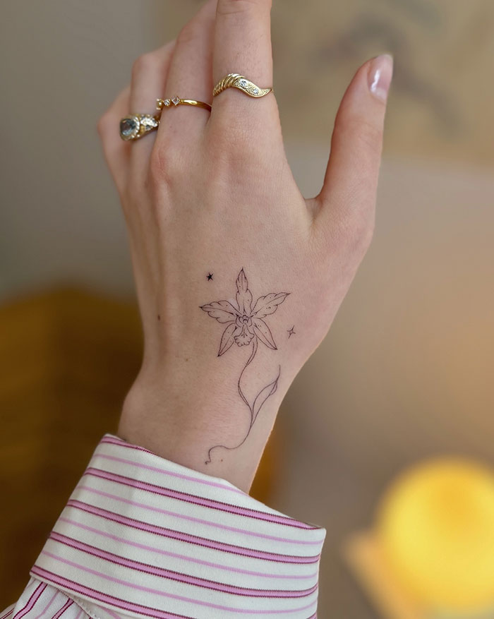 Delicate flower tattoo on woman's hand with gold rings, showcasing subtle tattoo ideas for women. 