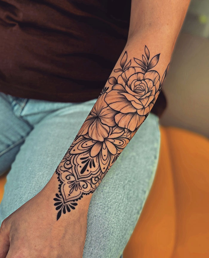 A tattoo idea for women with a floral tattoo design on a woman's forearm, featuring intricate patterns and bold lines.