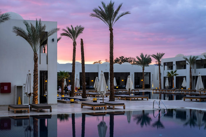 Luxury vacation hotel with palm trees and a pool at sunset.