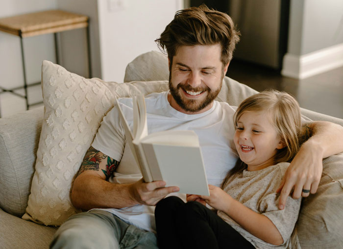 Man and child reading on couch, enjoying vacation time together.