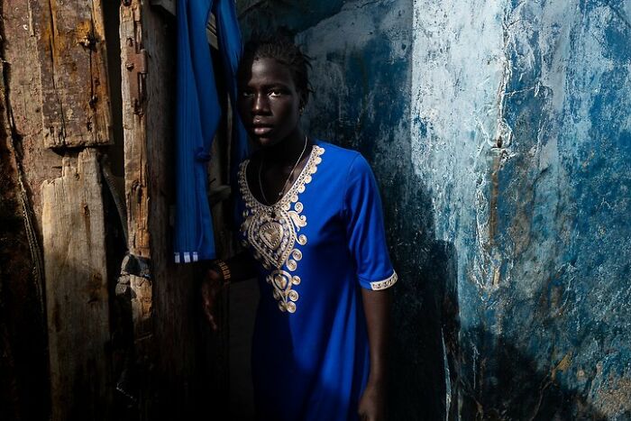 A person in a vibrant blue dress stands in a rustic setting, highlighting Ivan Margot's photography style.