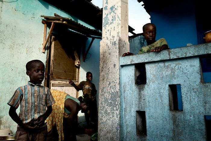 Children in a rustic setting against a blue backdrop, captured by Ivan Margot in a vibrant photograph.