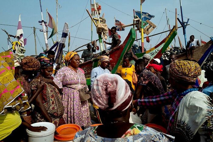 Vibrant photograph by Ivan Margot showing a lively market scene with colorful boats and people interacting.