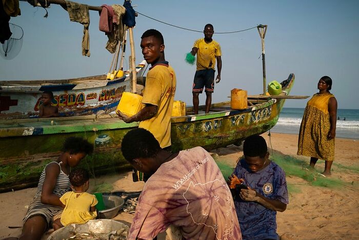 Fishermen and villagers at the beach with colorful boats, captured by Ivan Margot.