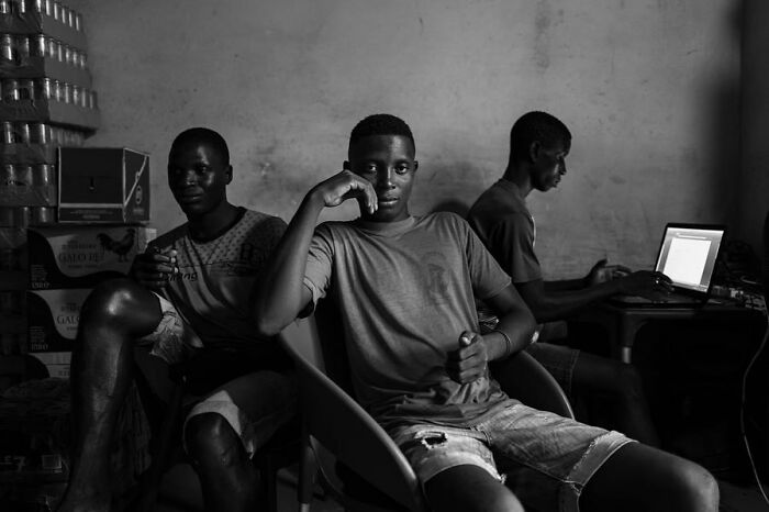 Three young men in a room, one talking on a phone and another using a laptop, capturing a moment in daily life.