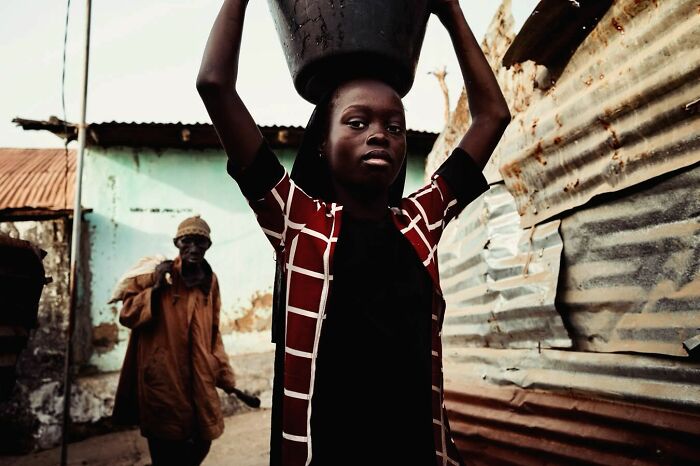 A vibrant photograph by Ivan Margot showing a person carrying a bucket on their head.