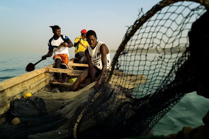 Fishermen in a boat pulling in fishing nets on a bright, sunny day. Photography by Ivan Margot.