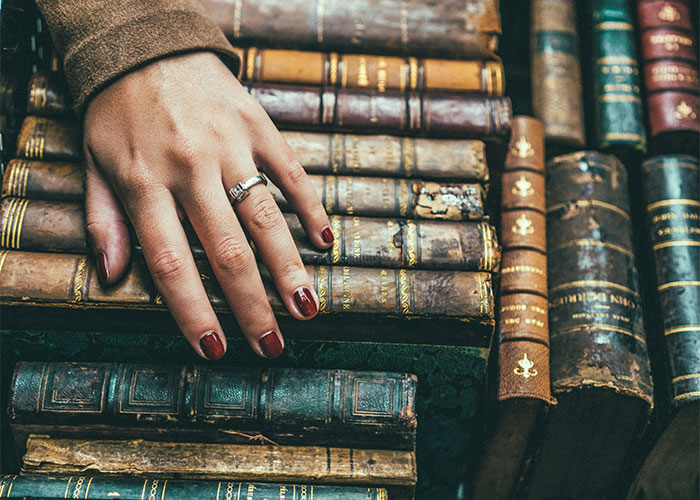 A hand with red nails rests on vintage books, hinting at unexplainable mystery.