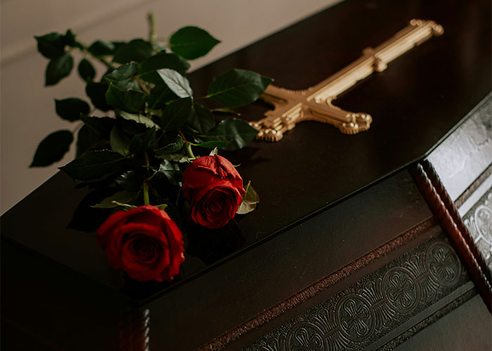 Red roses and a gold cross on a dark coffin, symbolizing an unexplainable mystery.