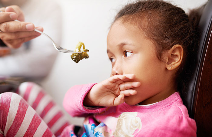 Child rejecting food with hand, looking away with displeasure.