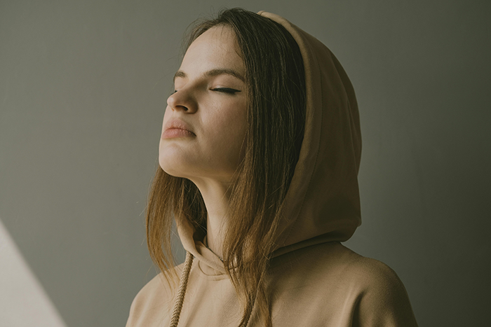 Woman in a tan hoodie with closed eyes, reflecting on relationship.