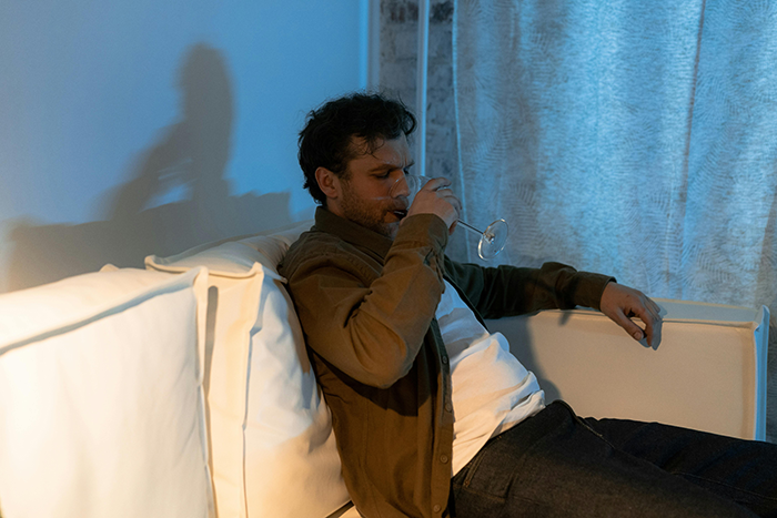 Man relaxing on a white sofa with a drink, contemplating a long relationship\'s end.