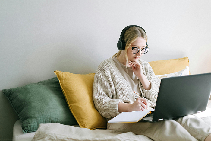 Woman in headphones sitting on a bed with a laptop, taking notes related to a hookup after a long relationship.