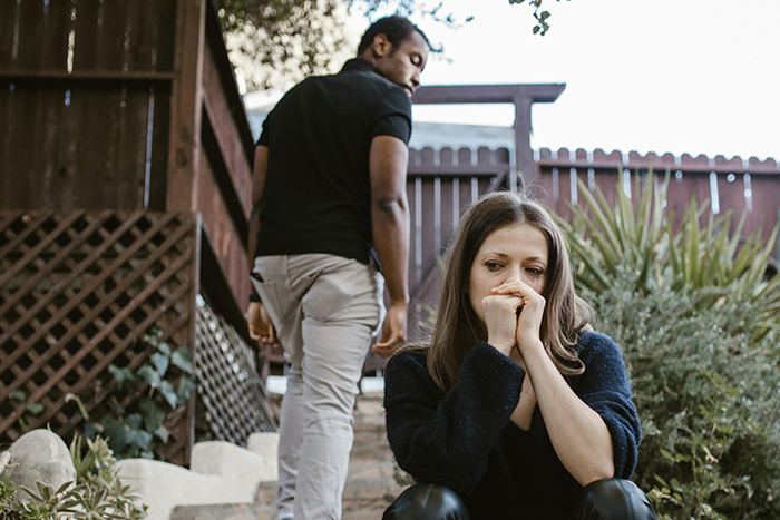 A thoughtful woman sits on stairs outside as a man walks away, illustrating a hookup ending a long relationship.