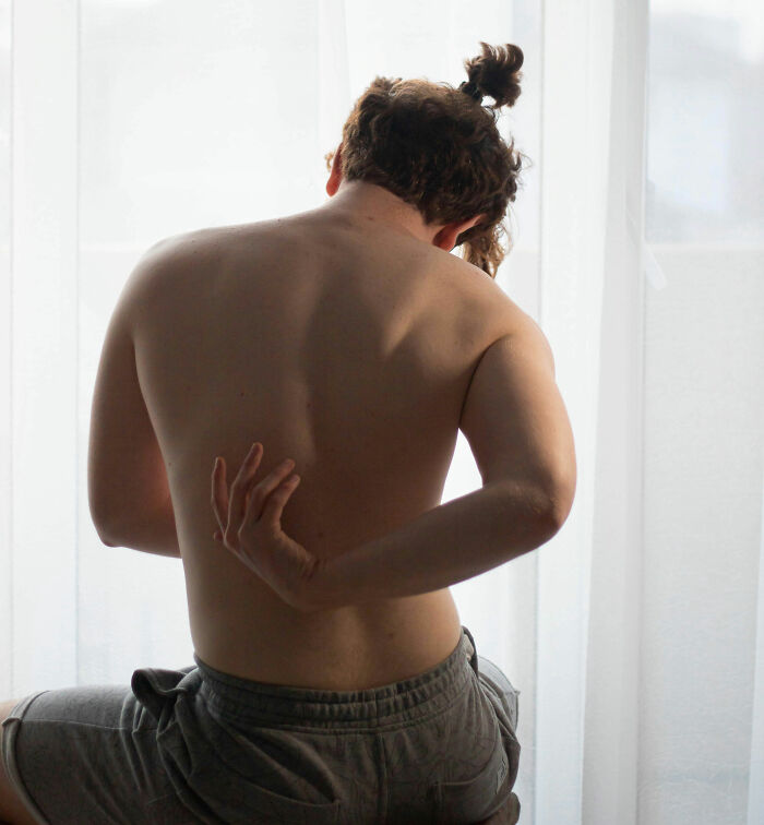 Person with back pain, holding their lower back, sitting against a light background.