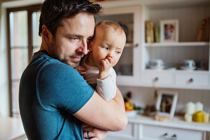 Dad babysits, holding a baby in a cozy kitchen setting.