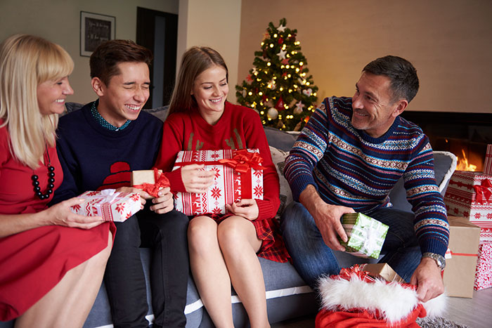 Family exchanging white elephant gifts by the Christmas tree.