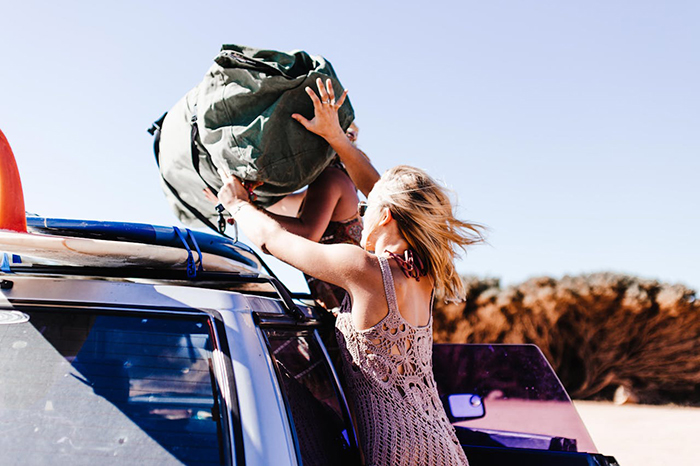 Person securing luggage on car roof for vacation, outdoors.