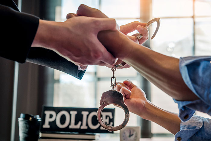 Police officer handcuffing a person with hands in close-up, related to roommate theft in an apartment.