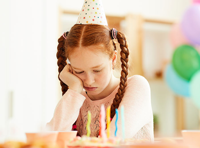 Girl wearing party hat, looking upset at a birthday table.