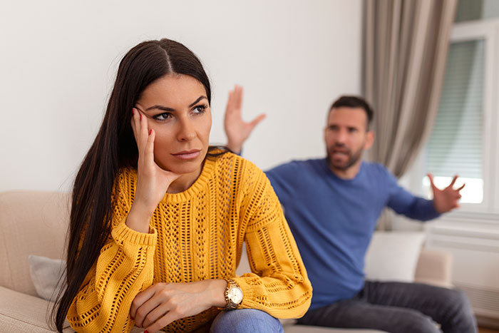 Woman in yellow sweater looking upset while man in blue shirt argues in the background, relating to husband affair baby conflict.