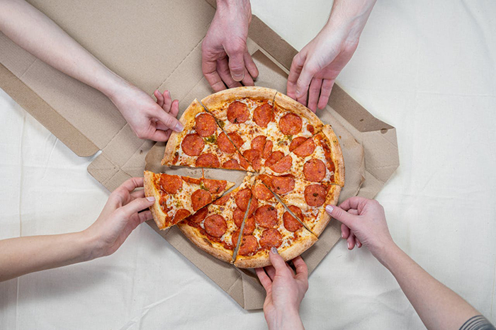 Hands reaching for slices of pepperoni pizza from a box, highlighting favorite pizza place dispute.