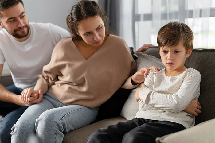 Woman comforting upset child on a sofa, concerned expression, while man sits beside her, related to party incident with stepdaughter.