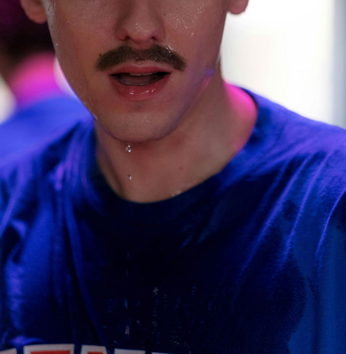 Man sweating in a blue shirt, showing genuine reaction.