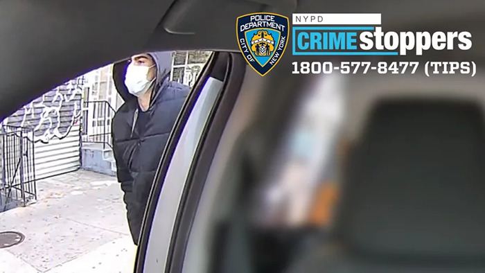 Masked individual in black jacket near a vehicle, NYPD Crimestoppers hotline visible, related to UnitedHealthcare CEO case.