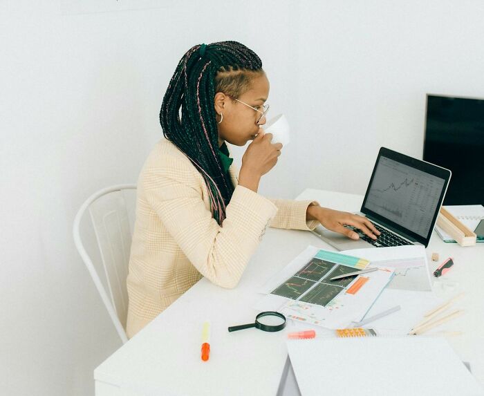 Person with "fun" job working at a desk, analyzing graphs on a laptop, with documents and a cup of coffee.