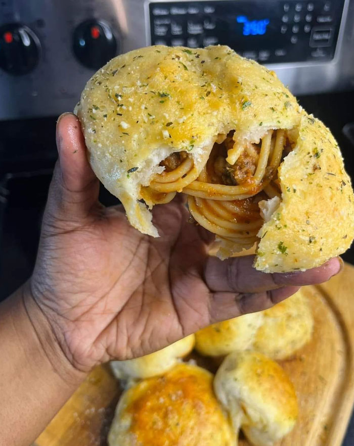 Hand holding a stuffed spaghetti garlic butter roll with spaghetti noodles visible inside.